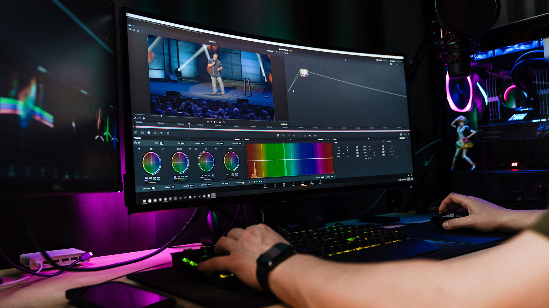 Person editing video on a curved monitor with color grading tools visible. Neon-lit PC setup creates a focused, creative atmosphere.